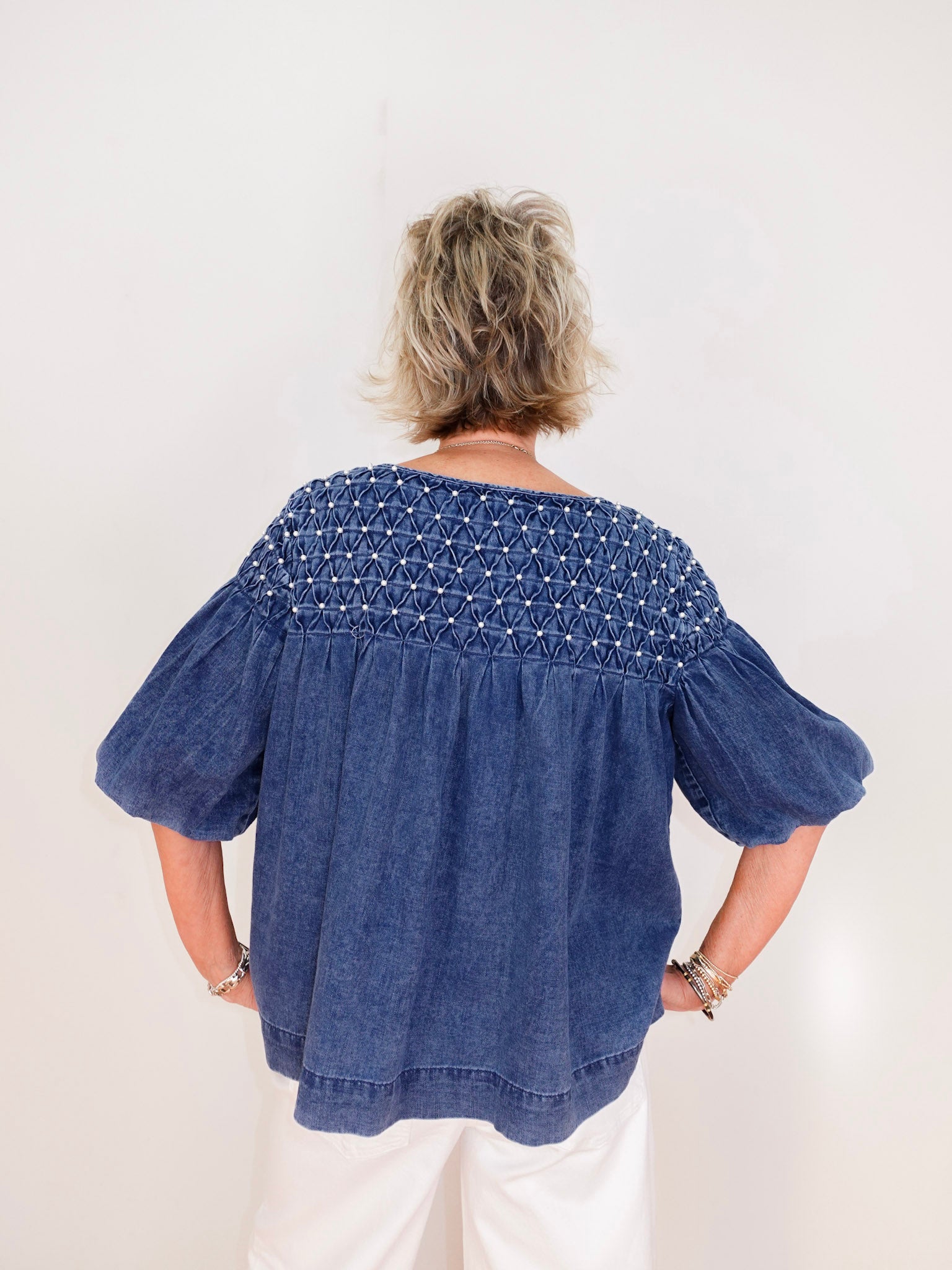 Person wearing a blue denim blouse with smocked details on a white background