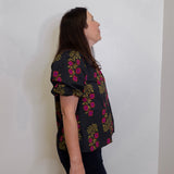 Woman wearing a black floral blouse against a white wall