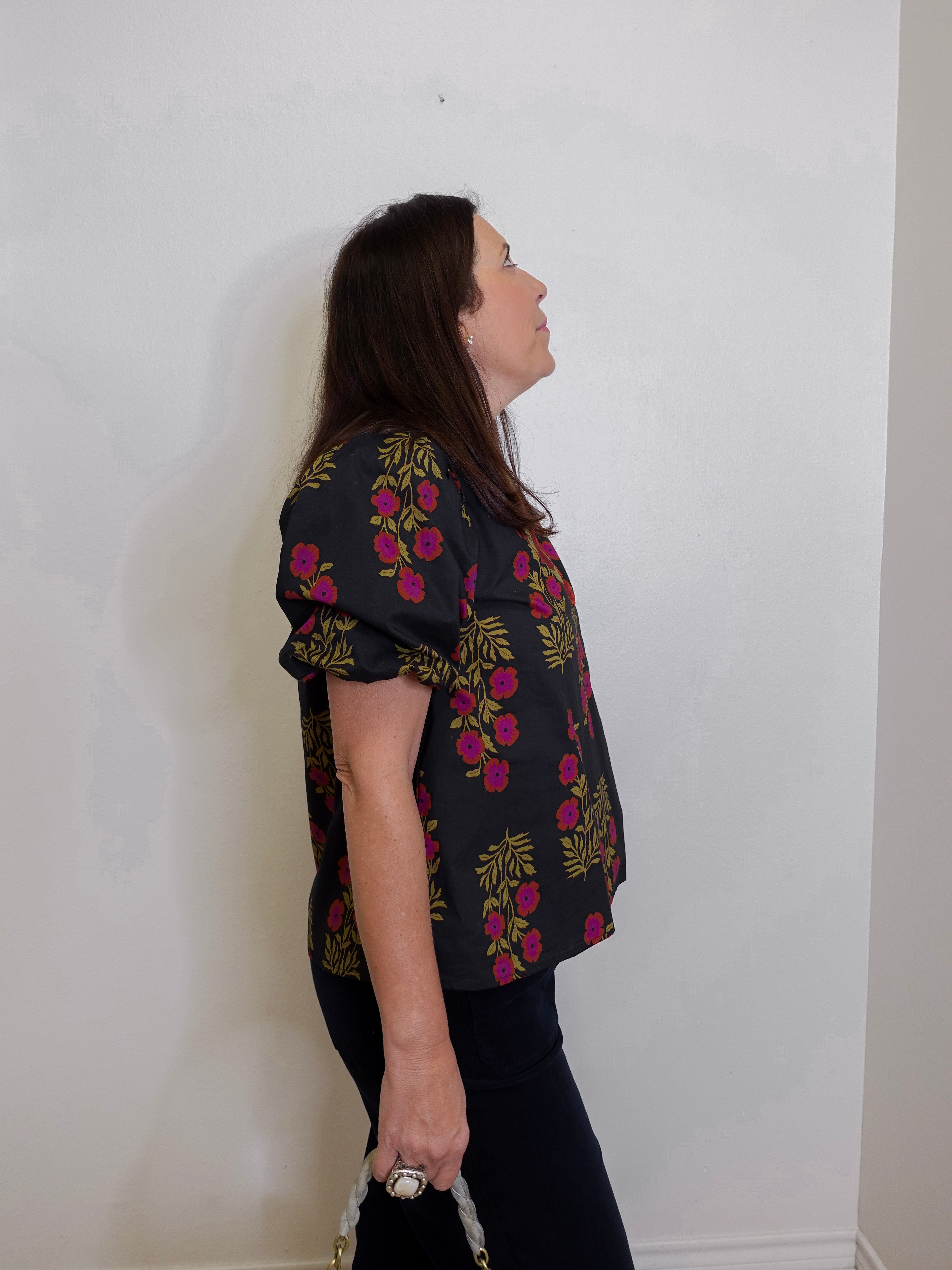 Woman wearing a black floral blouse against a white wall