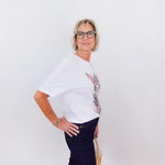 Person wearing a white top with floral sleeves and dark pants against a white background