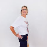 Person wearing a white top with floral sleeves and dark pants against a white background