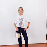 Woman wearing a graphic t-shirt with a cat design, dark jeans, and white sneakers against a white wall.