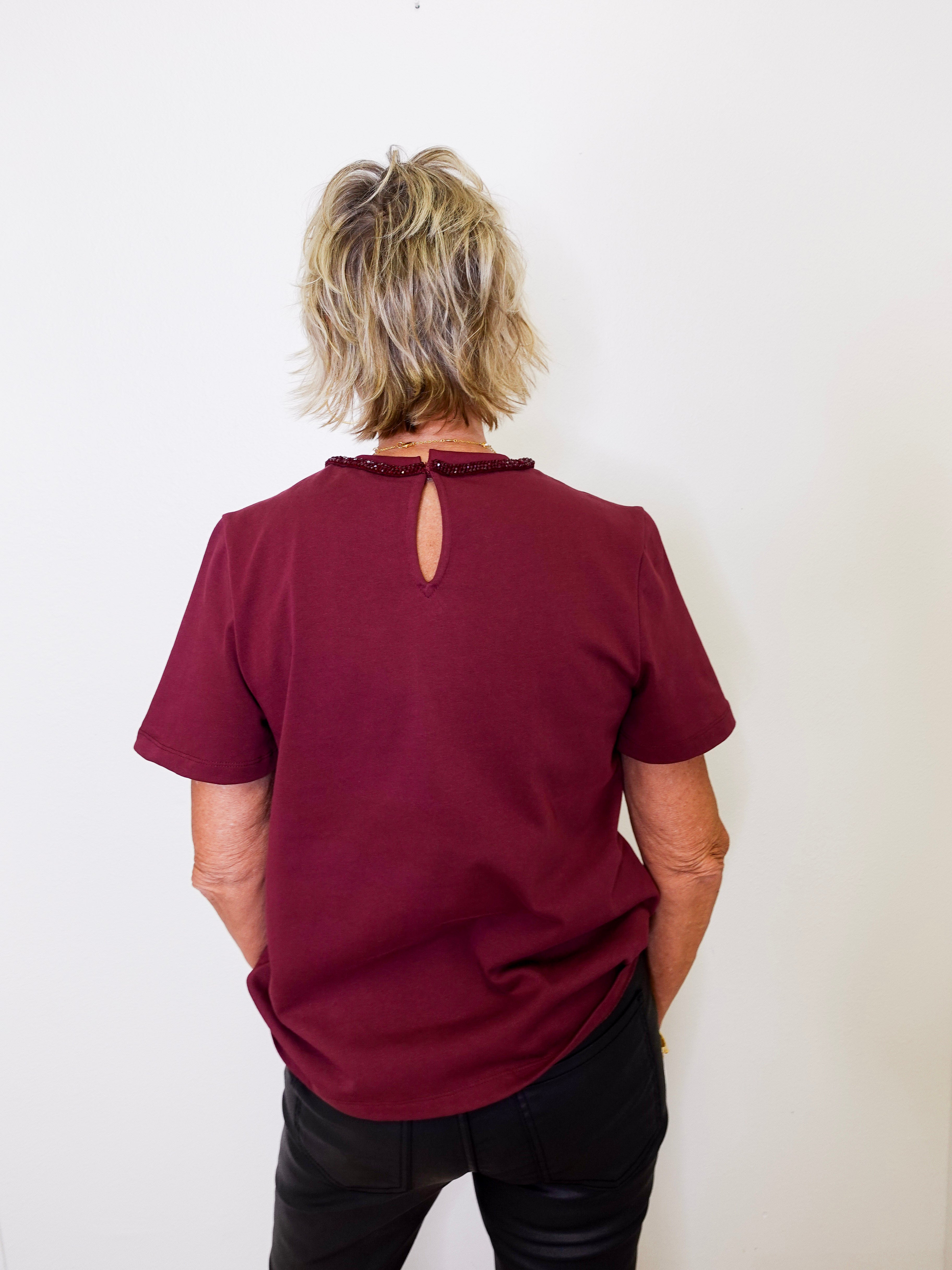 Person wearing a burgundy top with a cut-out back design against a white background