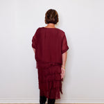 Person wearing a burgundy layered dress against a white wall.
