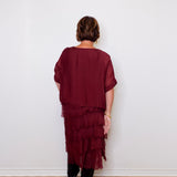 Person wearing a burgundy layered dress against a white wall.