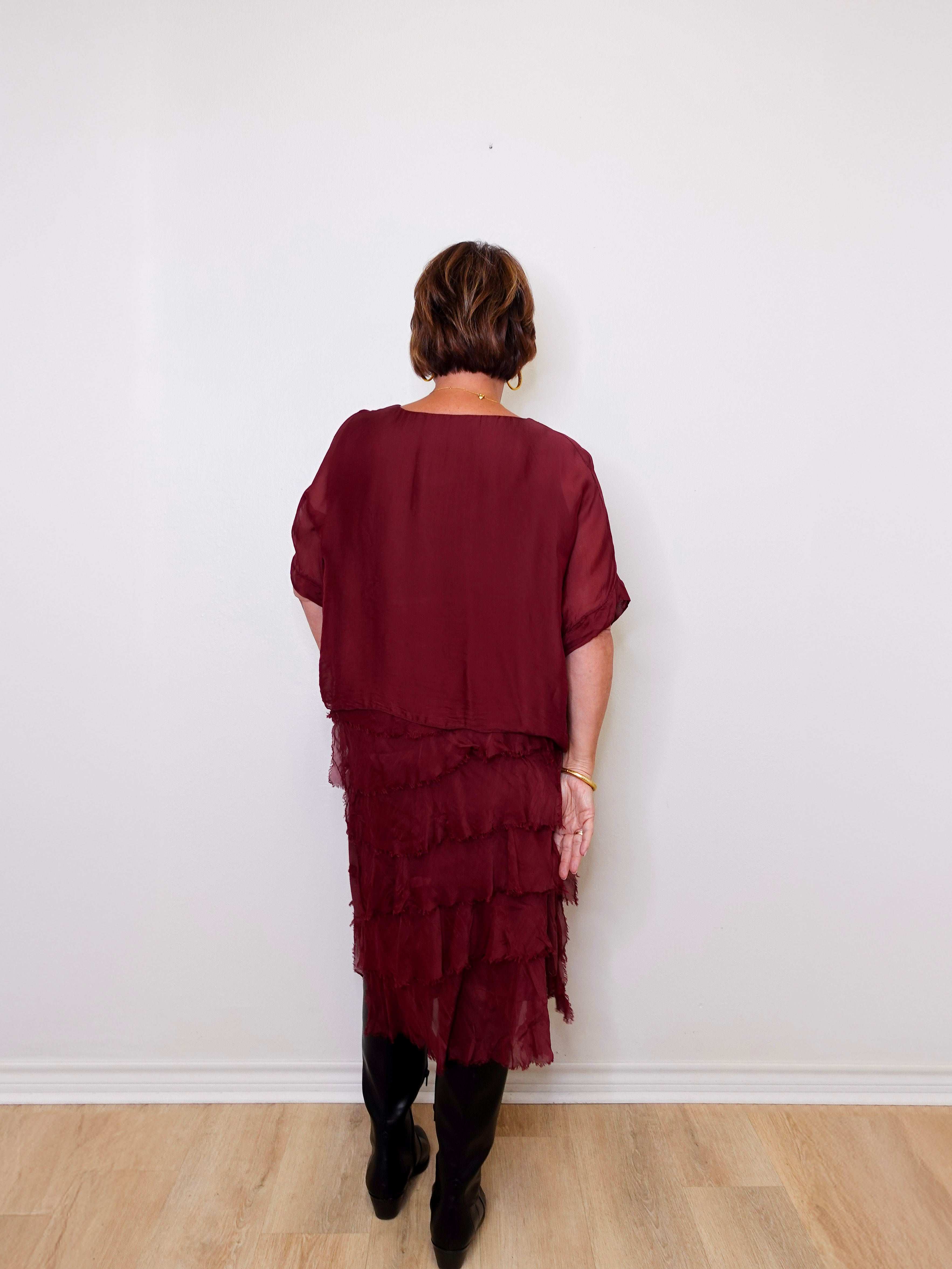 Person wearing a burgundy layered dress against a white wall.