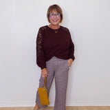 Woman wearing a burgundy sweater with lace sleeves and plaid pants, holding a yellow handbag against a white wall.