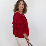 Woman wearing a red ruffled blouse and white skirt against a plain background