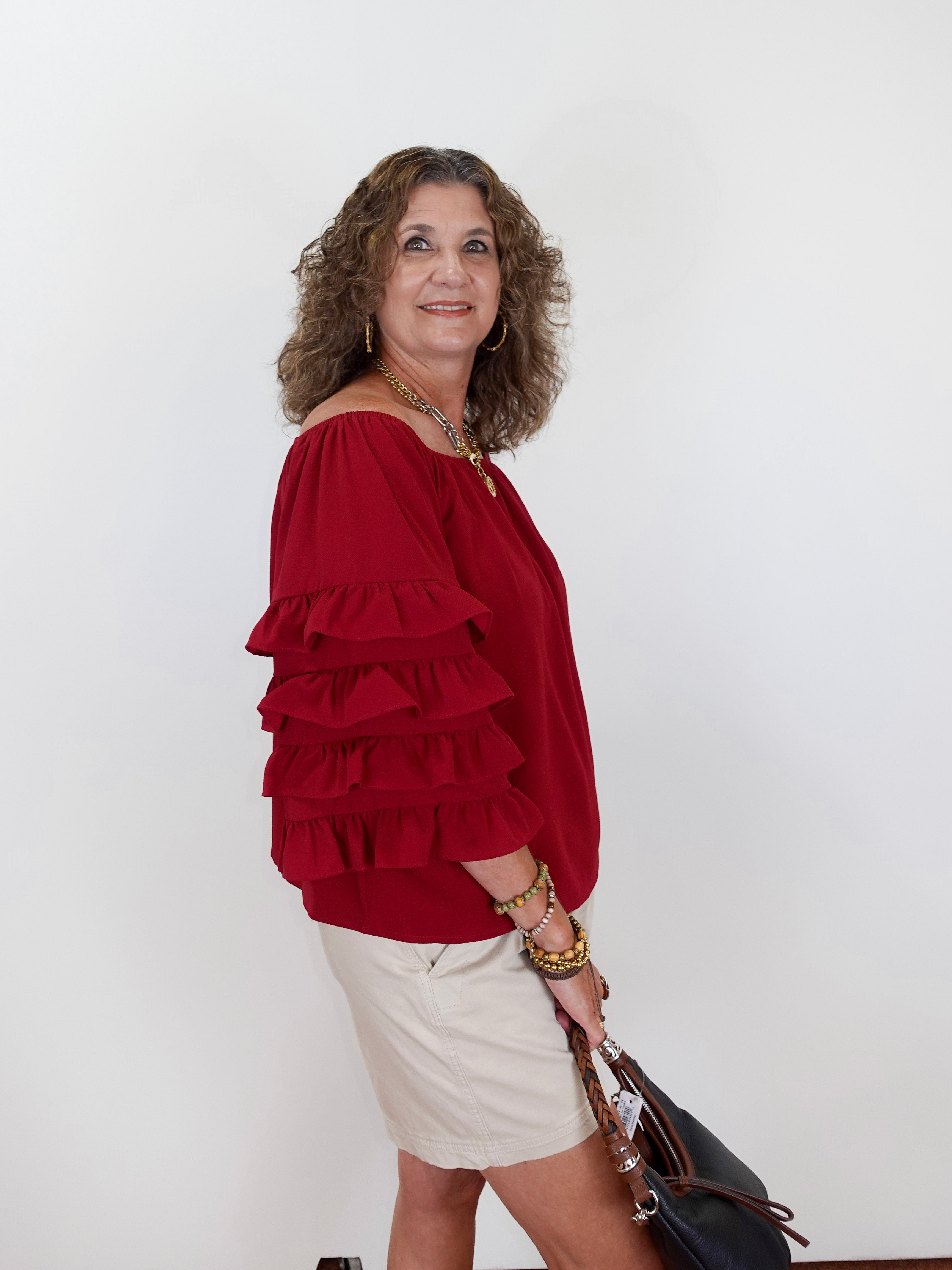 Woman wearing a red ruffled blouse and white skirt against a plain background
