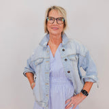 Woman wearing a light blue denim jacket over a striped dress against a plain background