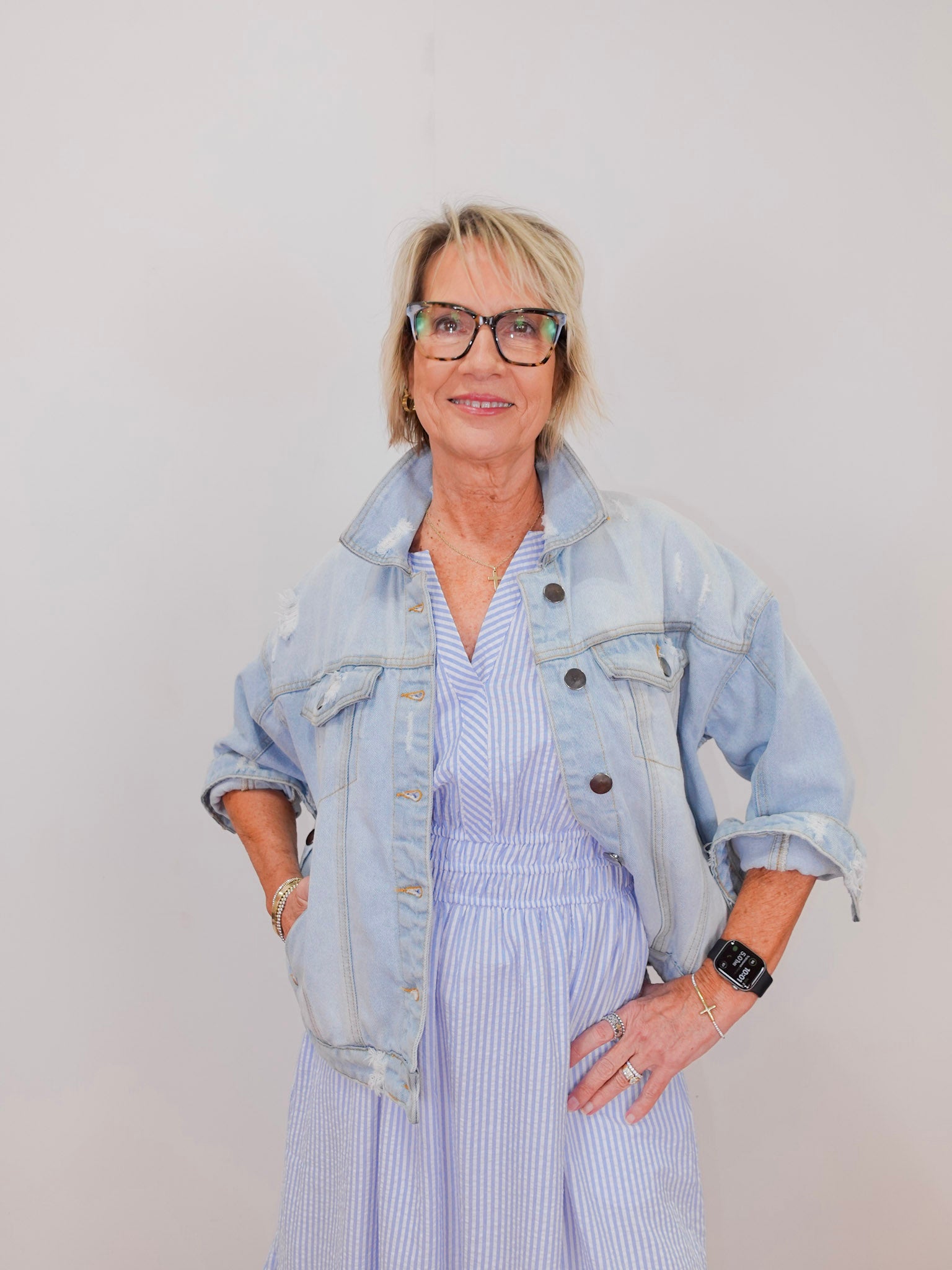 Woman wearing a light blue denim jacket over a striped dress against a plain background