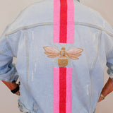 Light blue denim jacket with bee and striped design on the back, worn by a person.