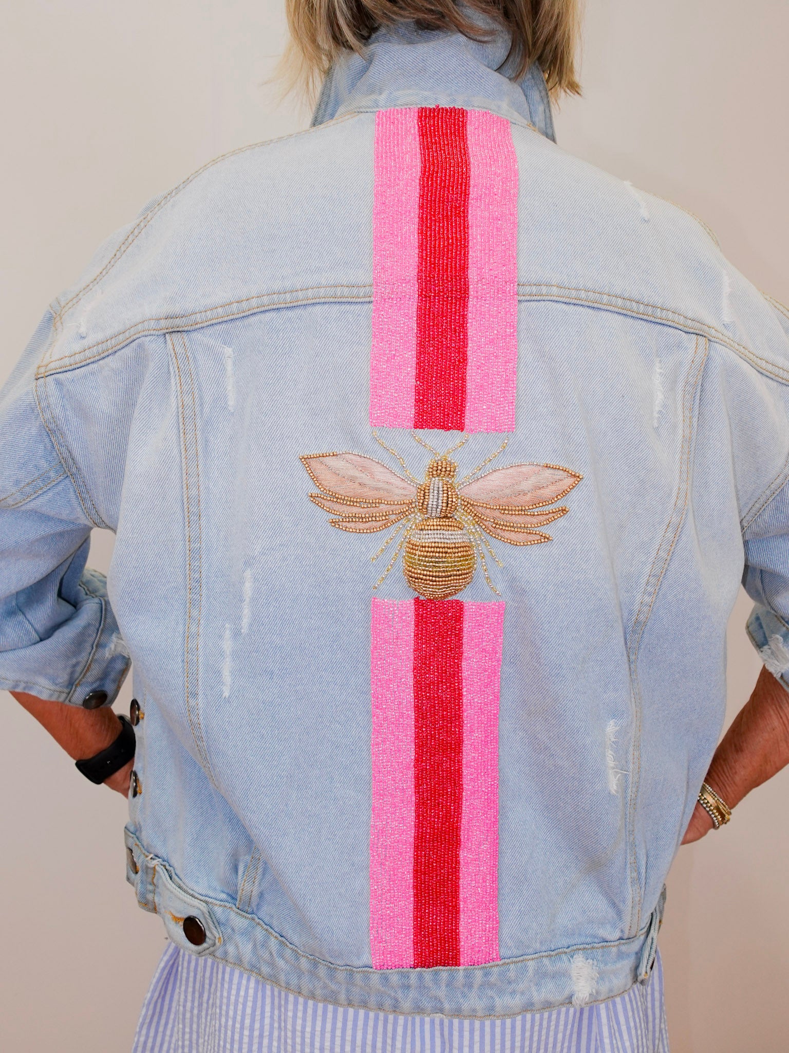 Light blue denim jacket with bee and striped design on the back, worn by a person.