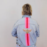 Person wearing a light blue denim jacket with pink stripes and a bee design on the back, standing against a plain background.