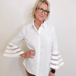 Woman wearing a white blouse with sheer sleeves against a plain background