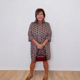 Woman wearing a patterned dress and red skirt against a white wall.