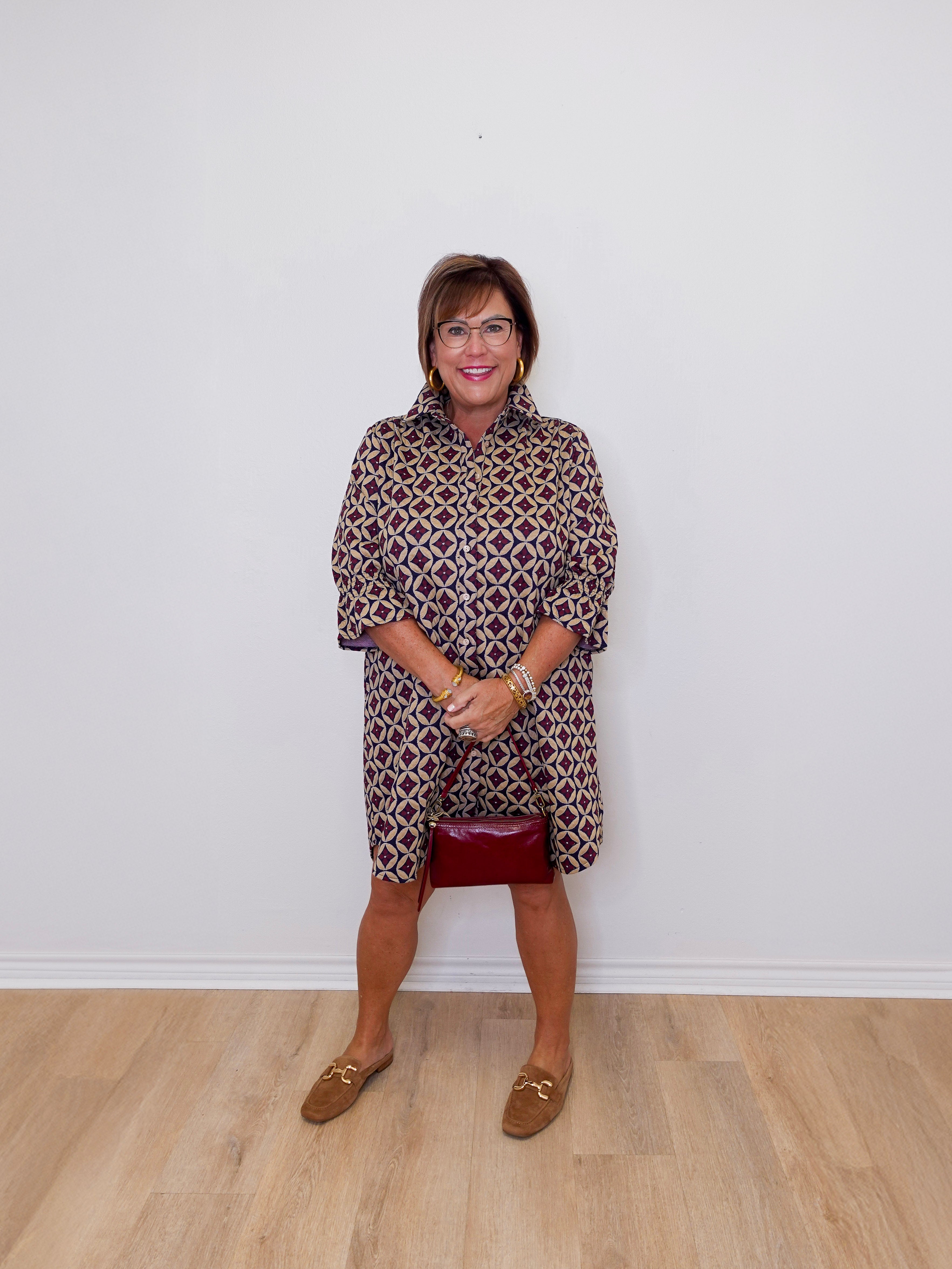 Woman wearing a patterned dress and red skirt against a white wall.