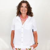 Woman wearing a white shirt and floral skirt with a pink necklace against a white background