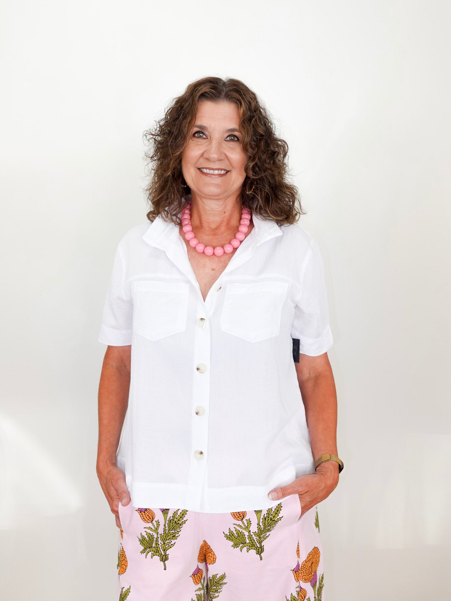 Woman wearing a white shirt and floral skirt with a pink necklace against a white background