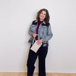 Woman wearing a denim jacket and black pants against a white wall