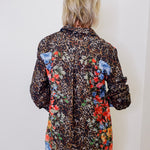 Person wearing a leopard print shirt with floral patches on a white background