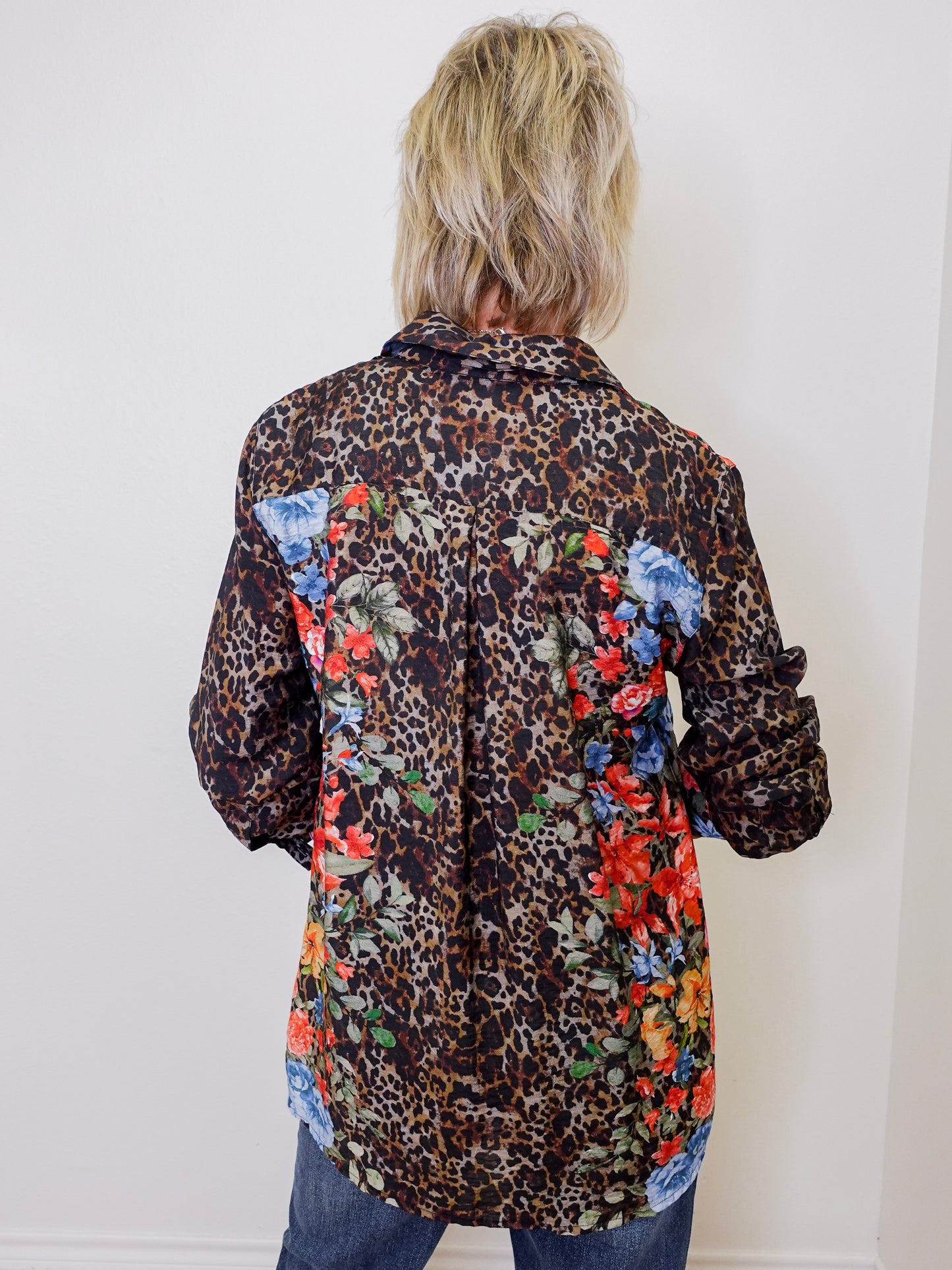 Person wearing a leopard print shirt with floral patches on a white background