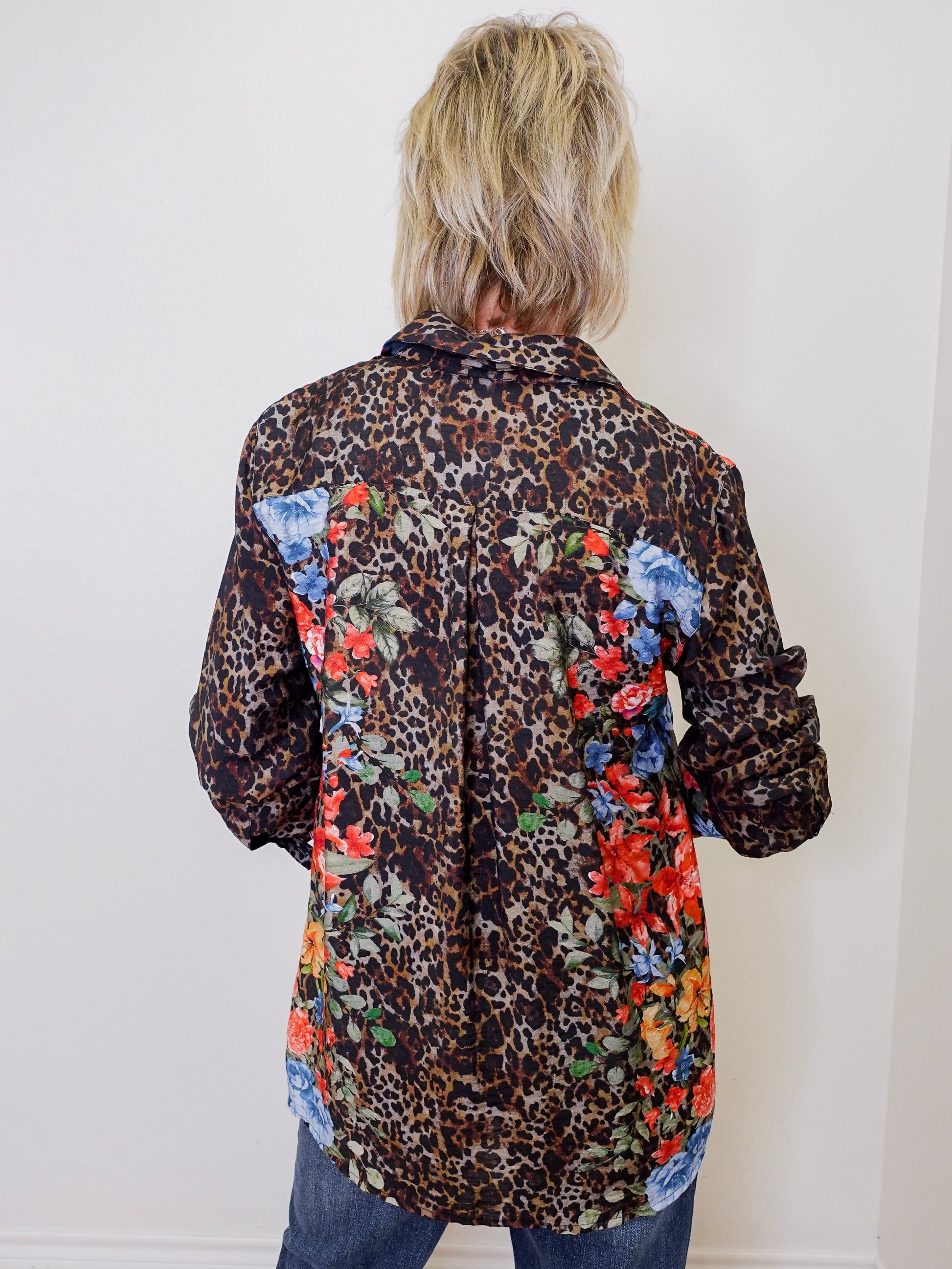 Person wearing a leopard print shirt with floral patches on a white background