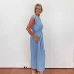 Woman wearing a light blue dress standing against a white wall.