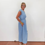 Woman wearing a light blue dress standing against a white wall.