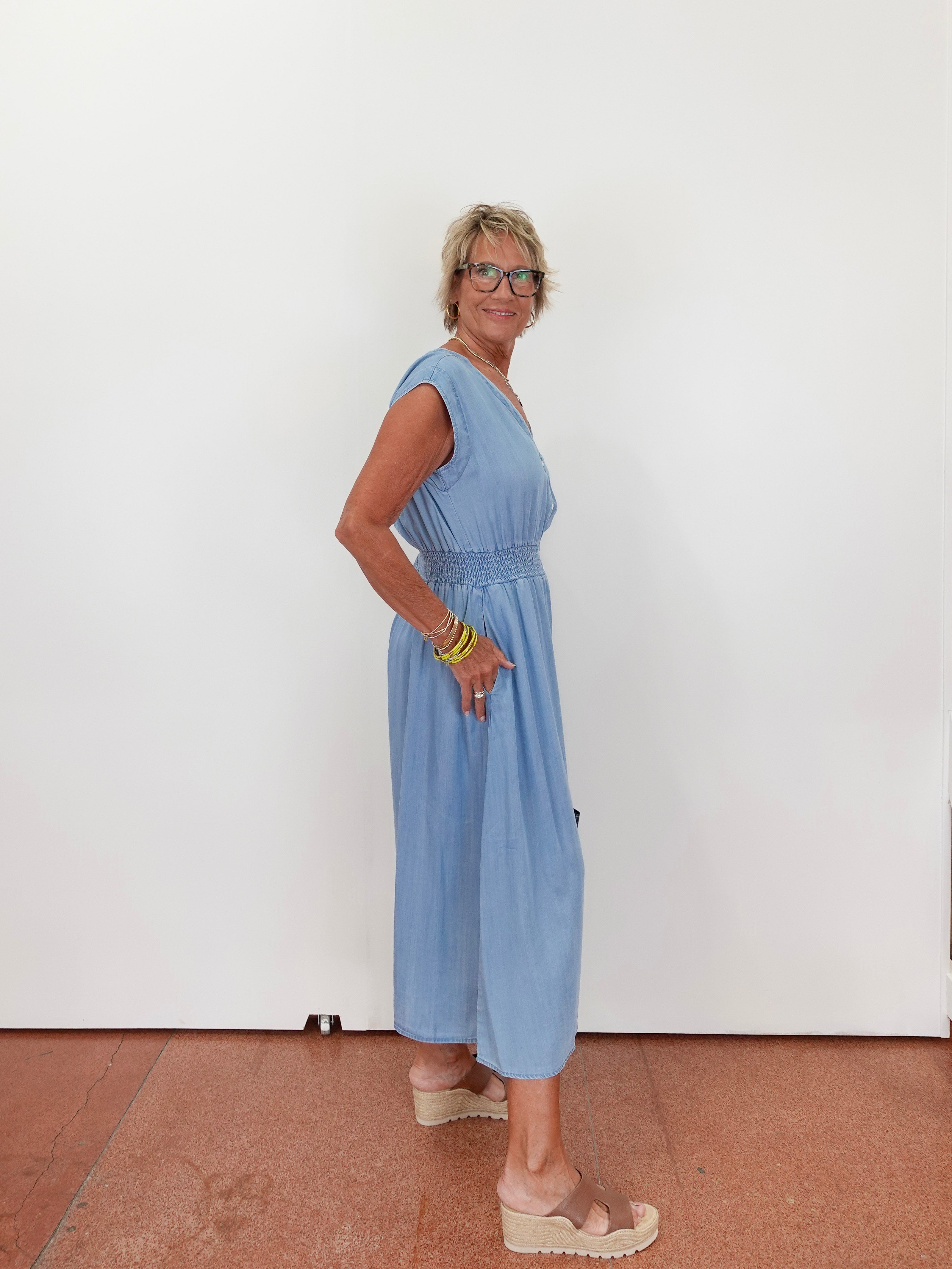 Woman wearing a light blue dress standing against a white wall.