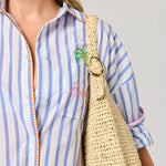 Person wearing a blue and white striped shirt with a straw bag featuring a logo.