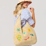 Woman wearing a straw bag with summer-themed embroidery on a plain background