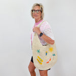 Woman holding a large woven bag with beach-themed designs against a white background