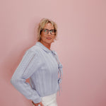 Woman wearing a light blue knitted sweater with a bow tie against a pink background