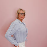 Woman wearing a light blue knitted sweater with a bow tie against a pink background