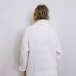 Person wearing a white knitted cardigan against a plain background
