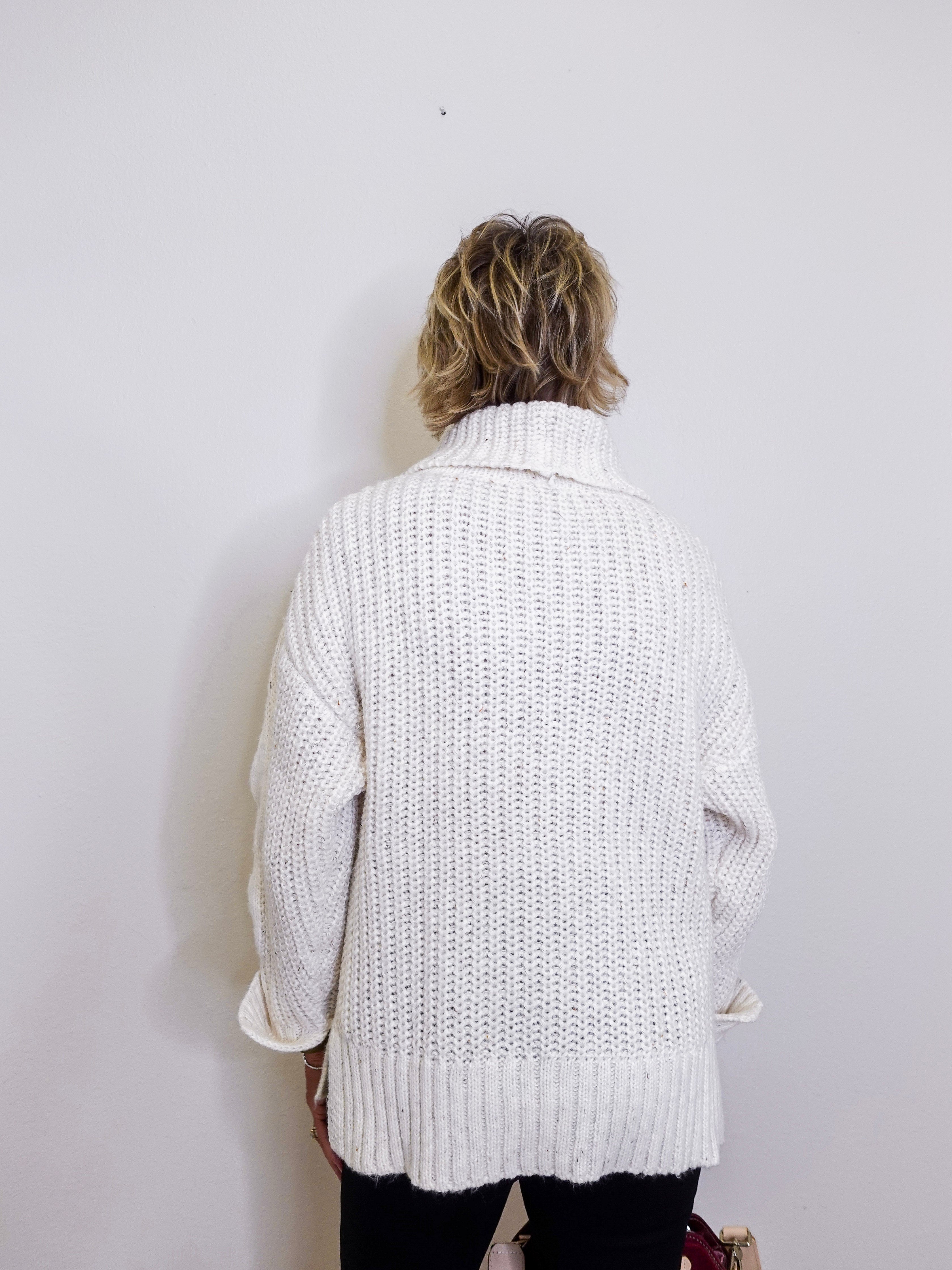 Person wearing a white knitted cardigan against a plain background