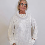 Woman wearing a white cable knit sweater against a plain background