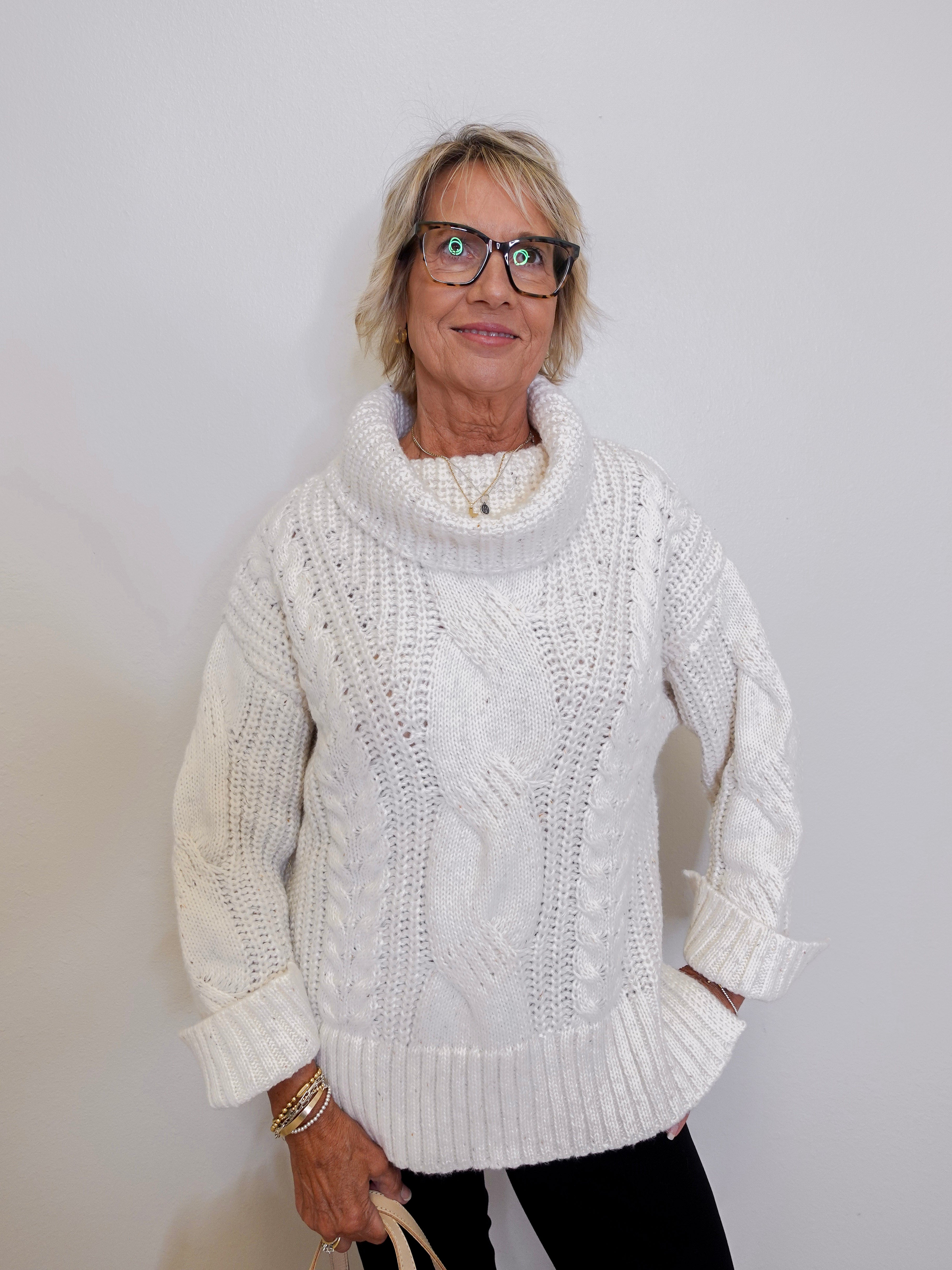 Woman wearing a white cable knit sweater against a plain background