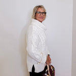 Woman wearing a white cable knit sweater against a plain background