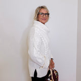 Woman wearing a white cable knit sweater against a plain background