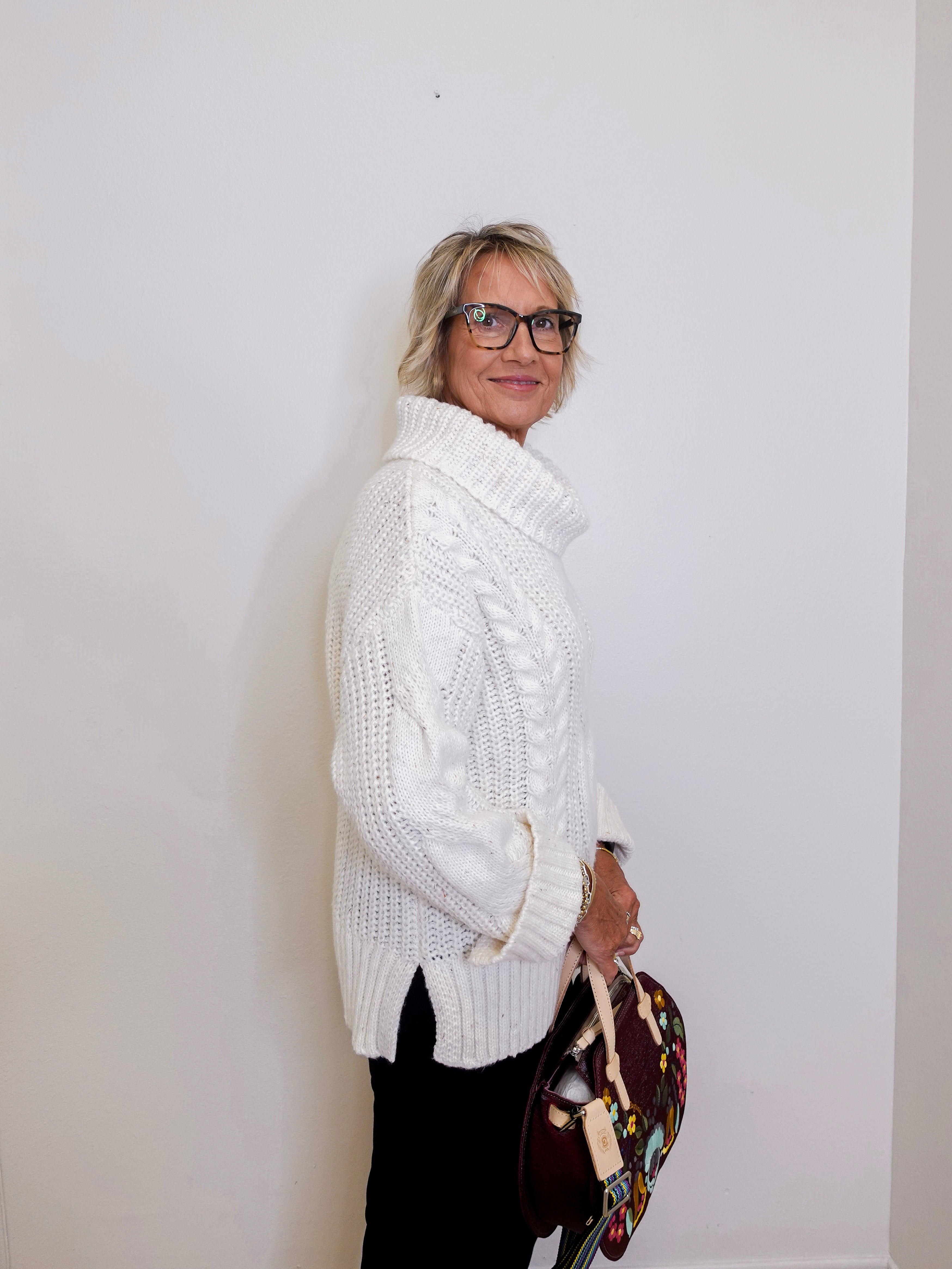 Woman wearing a white cable knit sweater against a plain background