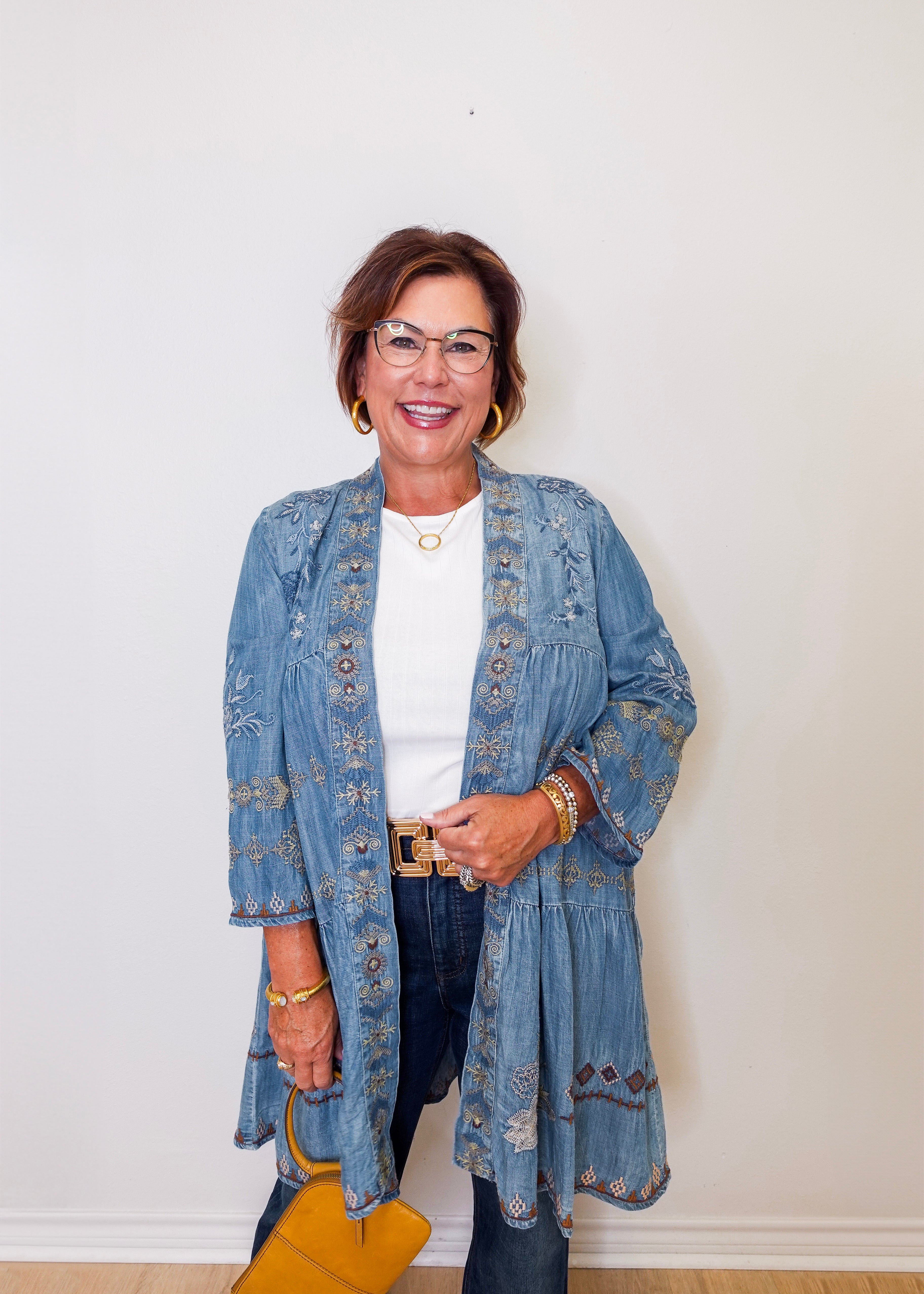 Woman wearing a blue embroidered jacket and denim jeans against a white wall