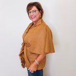 Woman wearing a brown cape over a light-colored shirt against a white wall.