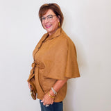 Woman wearing a brown cape over a light-colored shirt against a white wall.