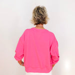 Person wearing a bright pink sweatshirt and white pants on a plain background