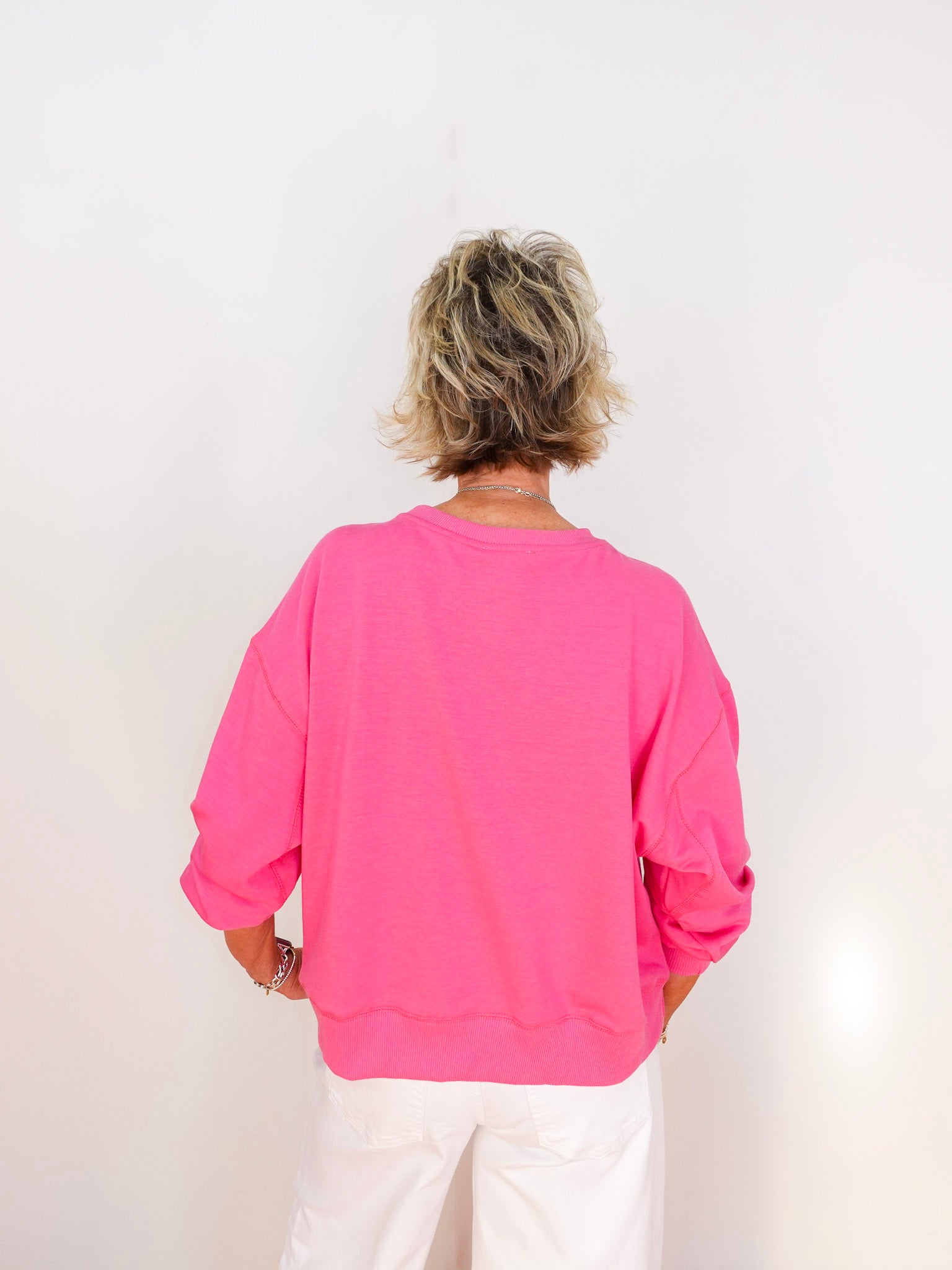 Person wearing a bright pink sweatshirt and white pants on a plain background