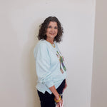 Woman wearing a light blue sweatshirt with a graphic design against a plain background