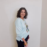 Woman wearing a light blue sweatshirt with a graphic design against a plain background