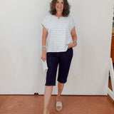 Woman wearing a striped shirt and navy shorts standing against a white wall.